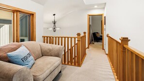 A hallway with a wooden railing, a sofa with a cushion, and a ceiling light fixture.