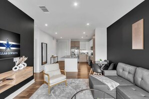 A modern living room with a sofa, a chair, a TV, and a kitchen in the background. - FriscoSquare+ToyotaStadium+Pool+Gym+PGAGolf+W+D (Frisco)