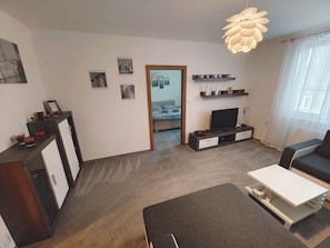 Ein modernes Wohnzimmer mit Sofa, Couchtisch, Fernseher und Bücherregal.
