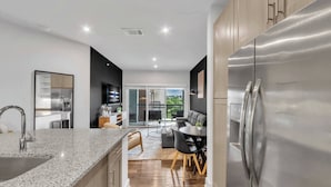 A modern kitchen with a stainless steel refrigerator, granite countertop, and a dining area with a round table and chairs. - Gym+Pool+FriscoSquare+ToyotaStadium+PGAGolf+W+D (Frisco)