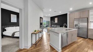 A modern kitchen with a central island, stainless steel appliances, and a dining area with a grey sofa. - Gym+Pool+FriscoSquare+ToyotaStadium+PGAGolf+W+D (Frisco)