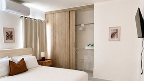 Et hotelværelse med seng, et natbord, et bruseområde og et ophængt fjernsyn.