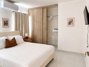 Ein Hotelzimmer mit Bett, Nachttisch, Duschbereich und einem an der Wand befestigten Fernseher.