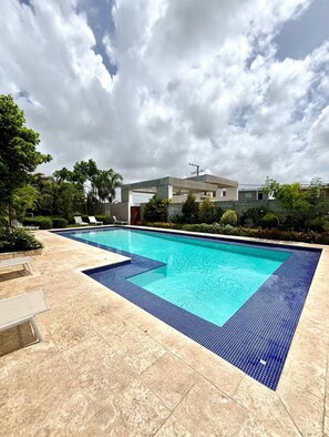 Une piscine rectangulaire dont le bord est recouvert de carreaux bleus, entourée d’une terrasse également carrelée.