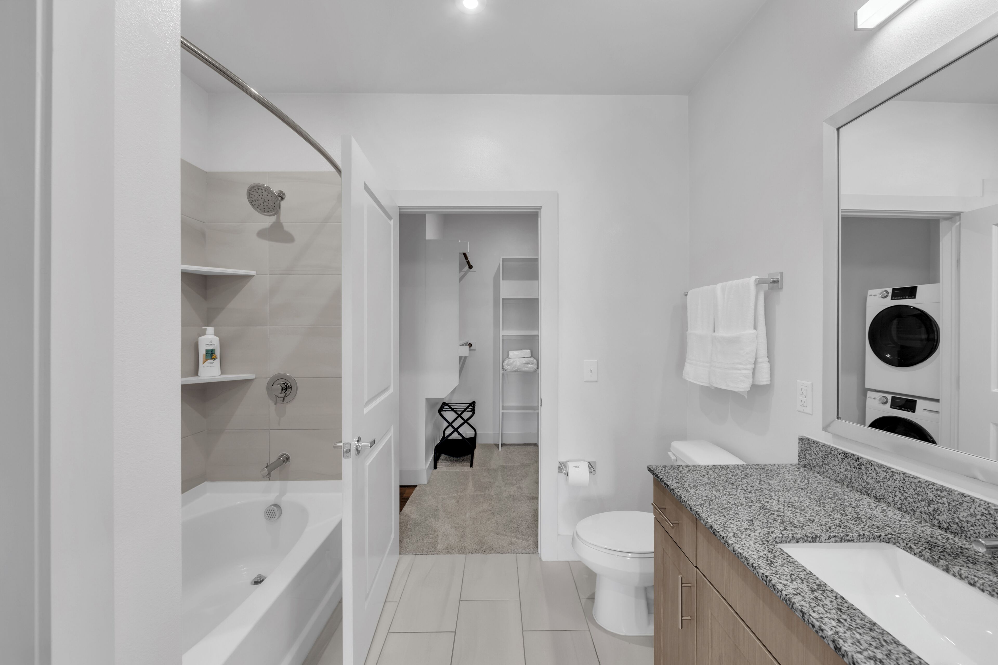 A modern bathroom with a bathtub, toilet, and sink, featuring a mirror, towel rack, and a shower area.