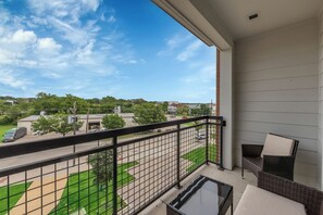 A balcony with a view of a street, a wicker chair, and a small table. - FriscoSquare+Gym+ToyotaStadium+Pool+PGAGolf+W+D (Frisco)