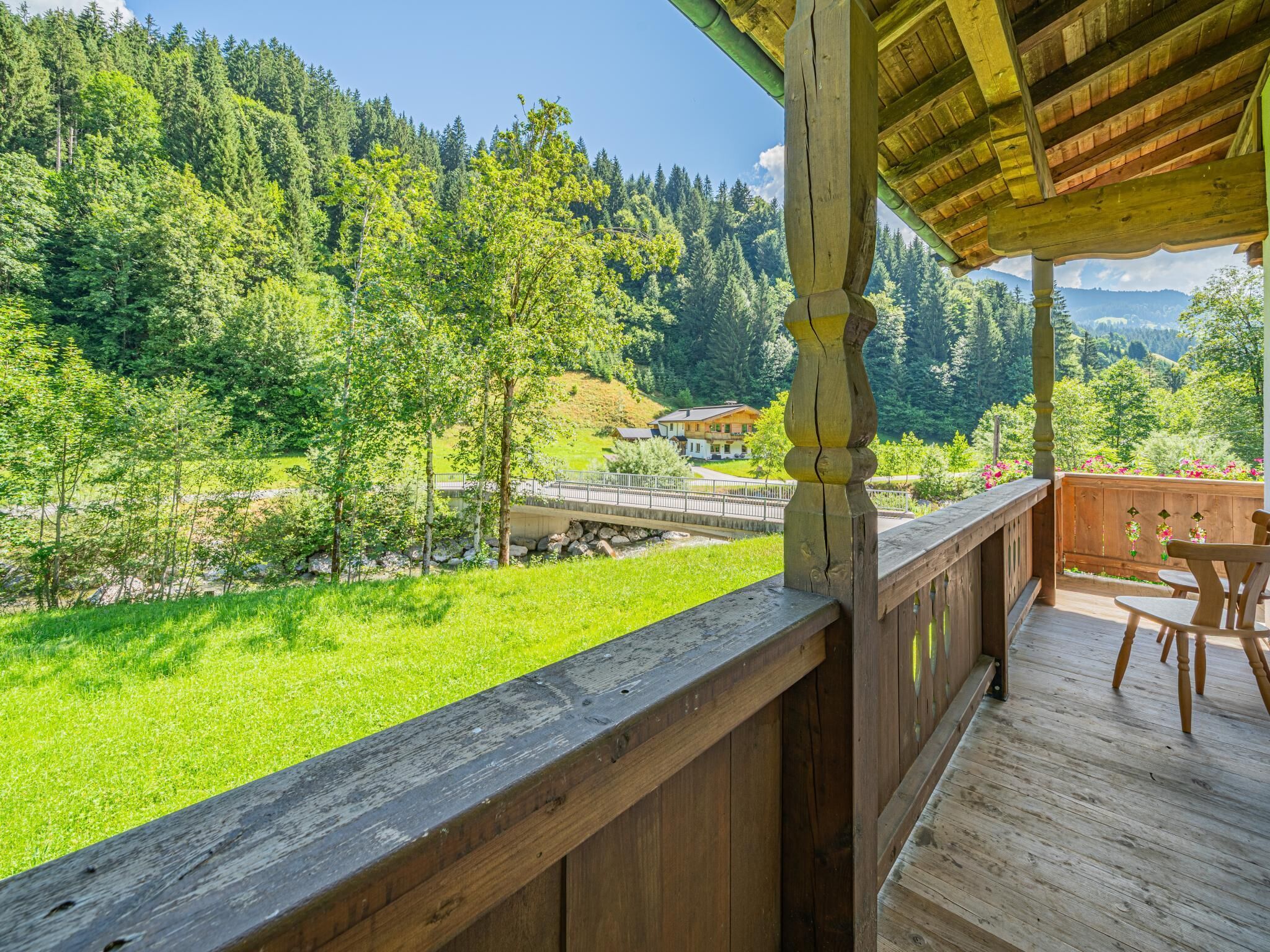 Eine Holzterrasse mit Blick auf einen Fluss, Bäume und ein Haus im Hintergrund.