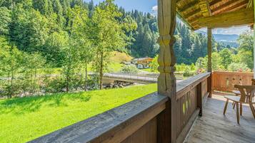 Eine Holzterrasse mit Blick auf einen Fluss, Bäume und ein Haus im Hintergrund.