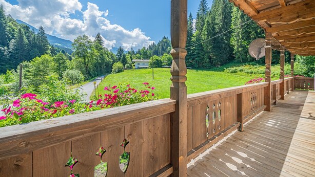 Eine Holzterrasse mit Blick auf eine grüne Landschaft, ein Haus im Hintergrund und einen klaren Himmel.