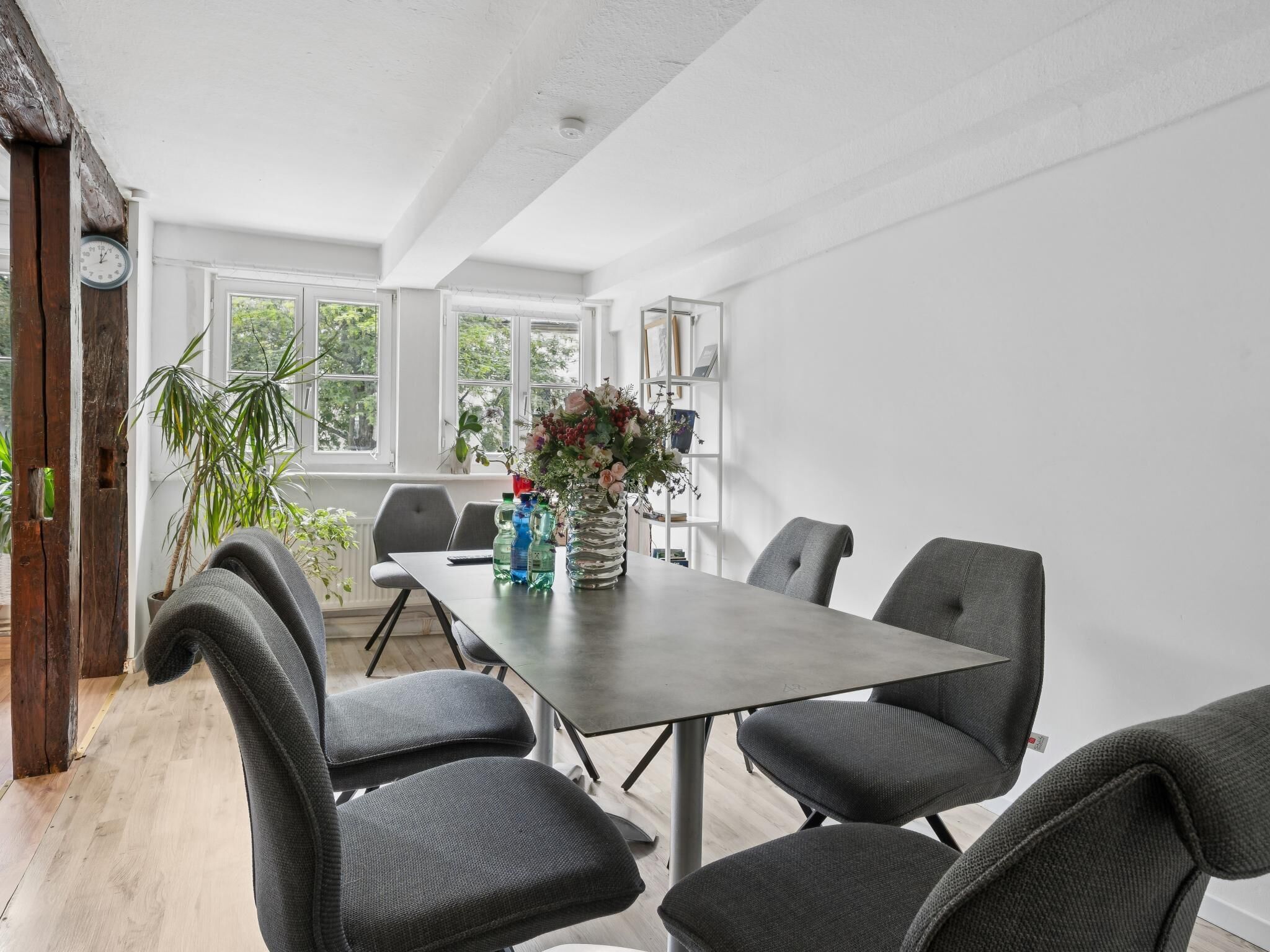 Un espace repas moderne avec une longue table, six chaises et un vase de fleurs.
