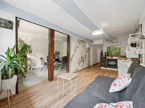 A modern living room with a grey sofa, a small white table, and a kitchen area with a stove and cabinets.