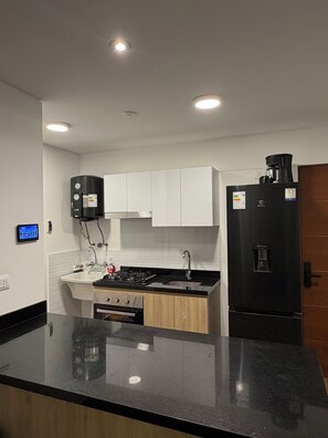 A modern kitchen with white cabinets, a black refrigerator, a stove, and a sink. - New Apartment in Miraflores (Miraflores)