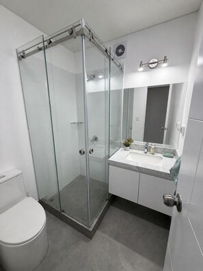 A modern bathroom with a glass-enclosed shower, a white toilet, and a sink with a marble countertop. - New Apartment in Miraflores (Miraflores)