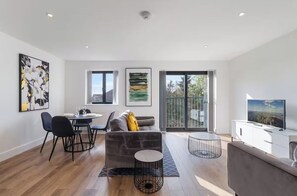 Ein modernes Wohnzimmer mit einer Couch, einem Esstisch, Stühlen, einem Fernseher und Kunstwerken an den Wänden.