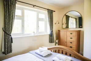 Um quarto com uma cama, cômoda de madeira, janela com cortinas e um espelho.