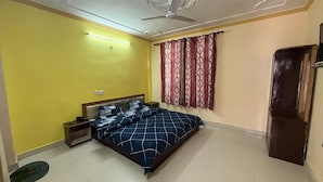 A bedroom with a bed, a nightstand, a ceiling fan, and a window with curtains. - Ghar by the mountains (Dharamshala)