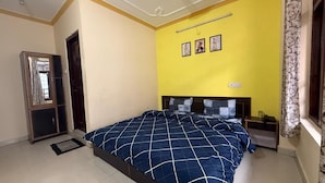 A bedroom with a bed, a nightstand, a window with curtains, and a door. - Ghar by the mountains (Dharamshala)