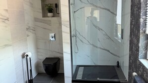 A modern bathroom with a glass-enclosed shower, marble walls, a black toilet, and a radiator. - Bella's Eden 1 romantic vacation in the countryside directly on the Mulde river (Grimma)