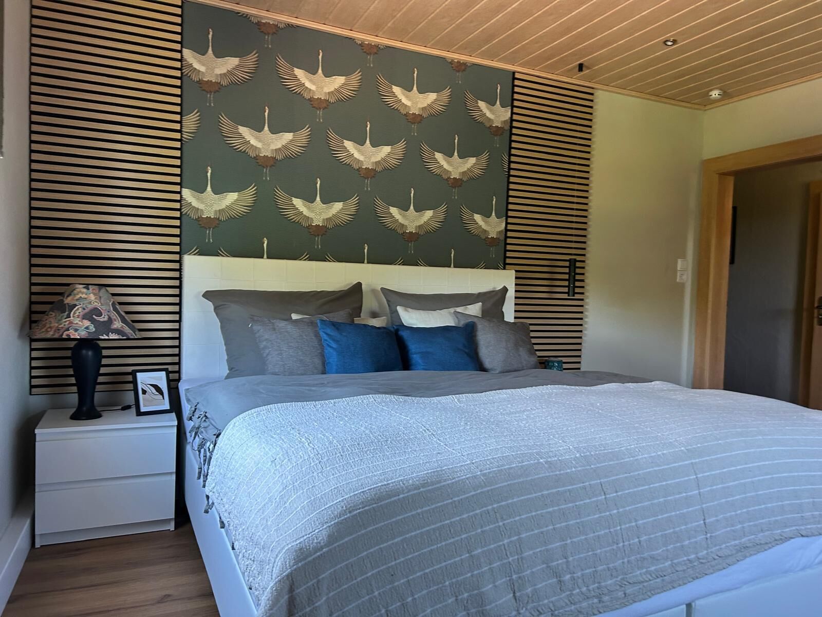 Ein Schlafzimmer mit einem Bett, Nachttischen, einer Lampe und einer Wand mit Vogelmuster.