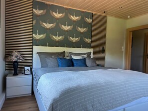 Une chambre à coucher comprenant un lit, des tables de chevet, une lampe et un mur orné d’un motif représentant des oiseaux.