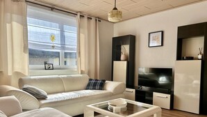 A modern living room with a sofa, coffee table, TV, and a window with curtains. - Bella's Eden 1 romantic vacation in the countryside directly on the Mulde river (Grimma)