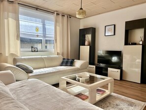 Ein modernes Wohnzimmer mit einer Couch, einem Couchtisch, einem Fernseher und einem Fenster mit Vorhängen.