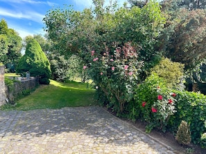 Un chemin pavé mène à un jardin luxuriant, où l’on trouve une variété de plantes et un mur de pierres.