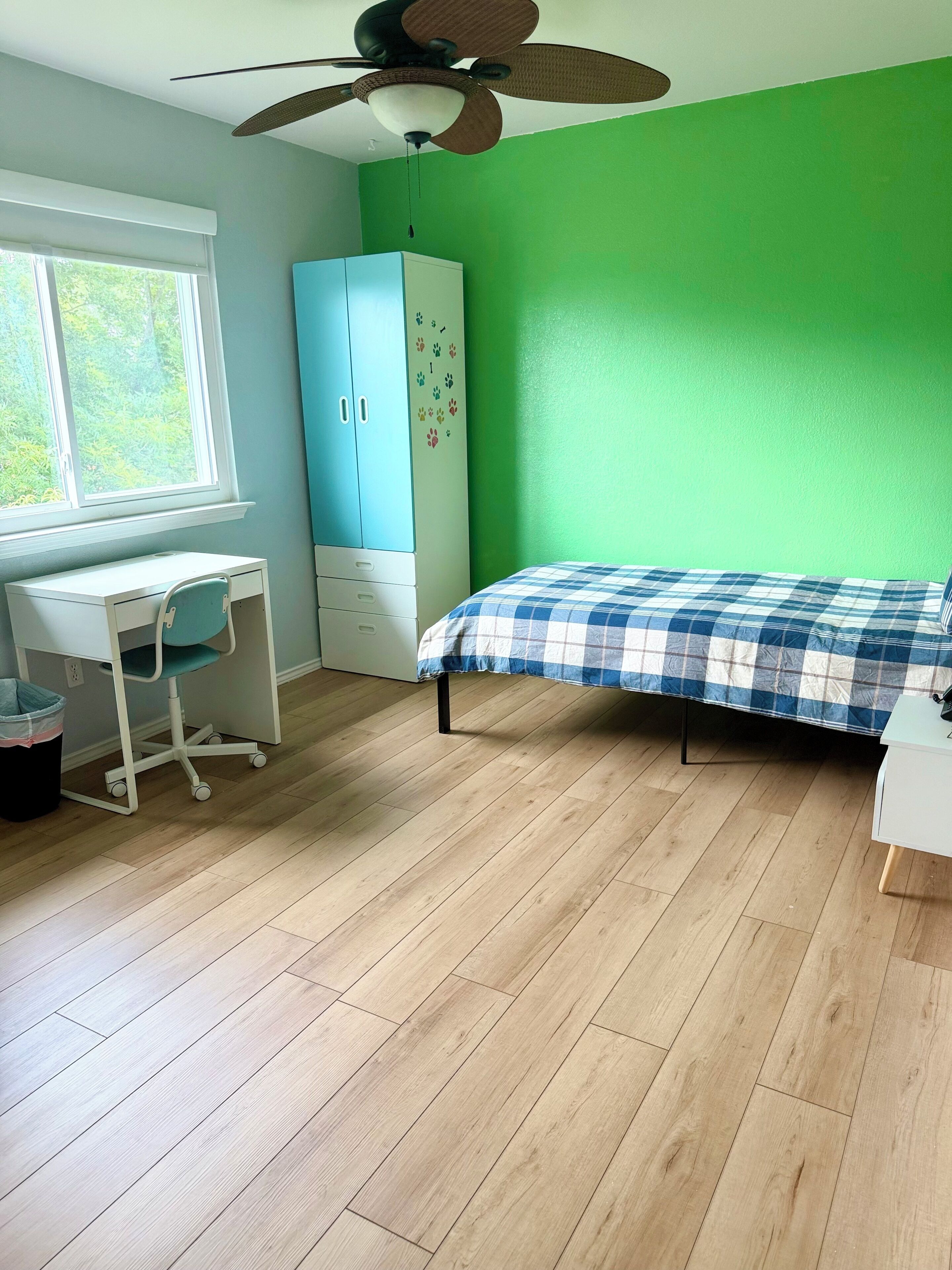 A bedroom with a bed, desk, chair, wardrobe, and a ceiling fan.