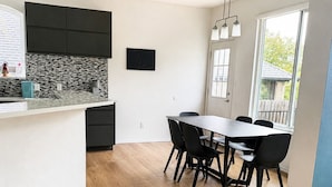 A modern kitchen with a central island, a dining area with a table and chairs, and a large window providing natural light. - 5BR Detached Casita with Massive Deck Sleeps 10 in Leander (Leander)