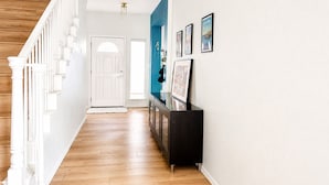 A hallway with a wooden staircase, a white door, and a black console table with framed pictures. - 5BR Detached Casita with Massive Deck Sleeps 10 in Leander (Leander)