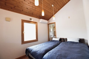 A bedroom with a wooden ceiling, a large window, a mirror, and a bed with blue bedding.