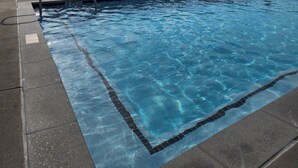 Een zwembad met helderblauw water, omgeven door een betonnen terras en metalen leuningwerken.
