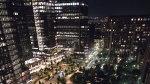 Luchtbeeld van een stad 's nachts, met hoogbouw, een centrale rotonde en een groen gebied.