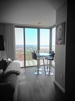 Ein modernes Hotelzimmer mit einer großen Schiebetür zum Balkon, einem Glastisch mit Stühlen, einer Couch und einem Bild an der Wand.