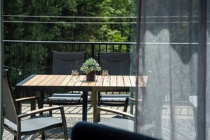Ein Holztisch mit Stühlen, einem Blumentopf und einem Glas auf einem Balkon mit Blick auf Bäume.