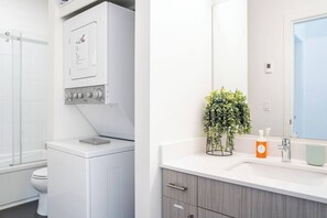 Ein modernes Badezimmer mit integrierter Waschmaschine und Trockner, einem großen Spiegel und einer Pflanze auf dem Waschtisch.