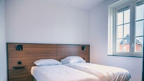 A bedroom with a wooden headboard, two bedside tables, a bed with white bedding, and a window with a view of houses. - Watervilla Wellness 8 (Medemblik)