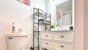 Ein Badezimmer mit Toilette, einem weißen Waschtisch mit Schubladen, einem schwarzen Metallregal und einem Spiegel über dem Waschtisch.