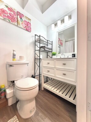 Ein Badezimmer mit Toilette, einem weißen Waschtisch mit Schubladen, einem schwarzen Metallregal und einem Spiegel über dem Waschtisch.