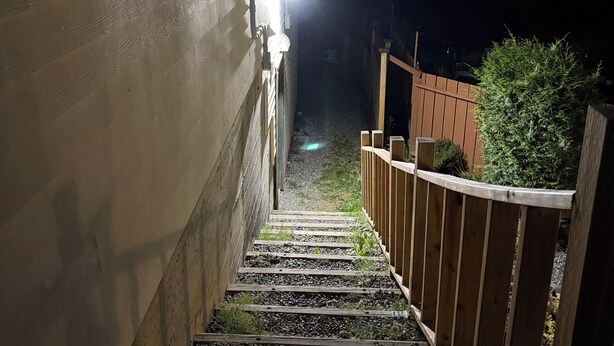Eine Holztreppe führt zu einem Haus, dessen oberstes Geschoss beleuchtet ist.