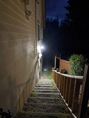 Eine Holztreppe führt zu einem Haus, dessen oberstes Geschoss beleuchtet ist.