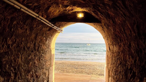 Een tunnel die naar een strand leidt, met een boot in de verte.