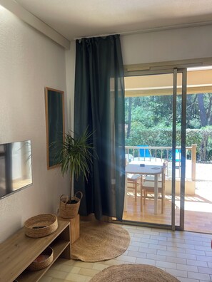 A room with a TV, a plant, a table, and a view of an outdoor patio. - Pool studio with beach access (Sanary-sur-Mer)