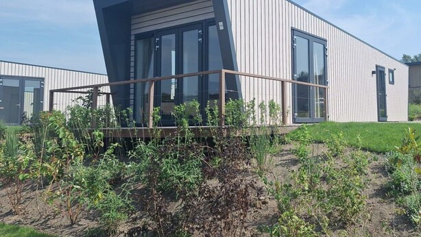 A modern building with a sloped roof, large windows, and a wooden deck. - Just Nature Light 4 (Olburgen)