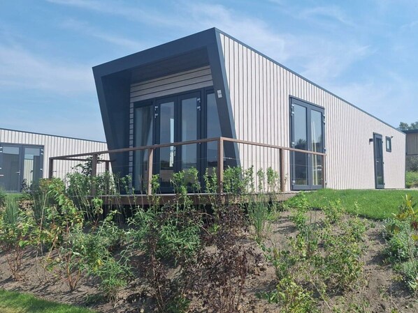 A modern building with a sloped roof, large windows, and a wooden deck. - Just Nature Light 4 (Olburgen)