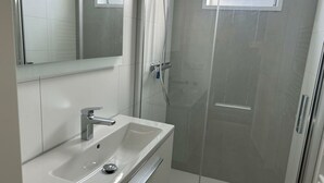 A bathroom with a white sink, mirror, and shower enclosure. - Just Nature Light 4 (Olburgen)
