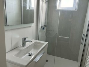 A bathroom with a white sink, mirror, and shower enclosure. - Just Nature Light 4 (Olburgen)
