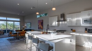 Una cocina moderna con una isla grande, armarios blancos y un comedor con taburetes de bar.