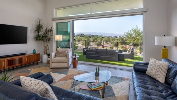 Una sala de estar moderna con un televisor de pantalla plana, un sofá, una mesa de centro y vistas a un área exterior ajardinada.