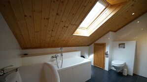 Un baño moderno con tragaluz, una bañera independiente, inodoro y lavabo.